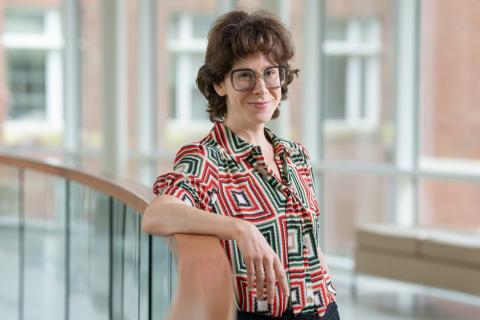 A photo of a white woman with glasses leaning against a half wall.